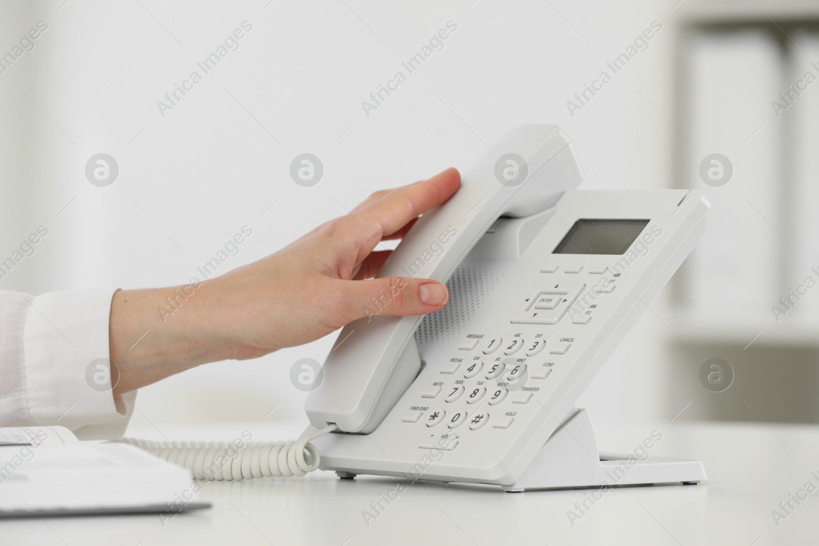 Photo of Assistant taking telephone handset at white table, closeup
