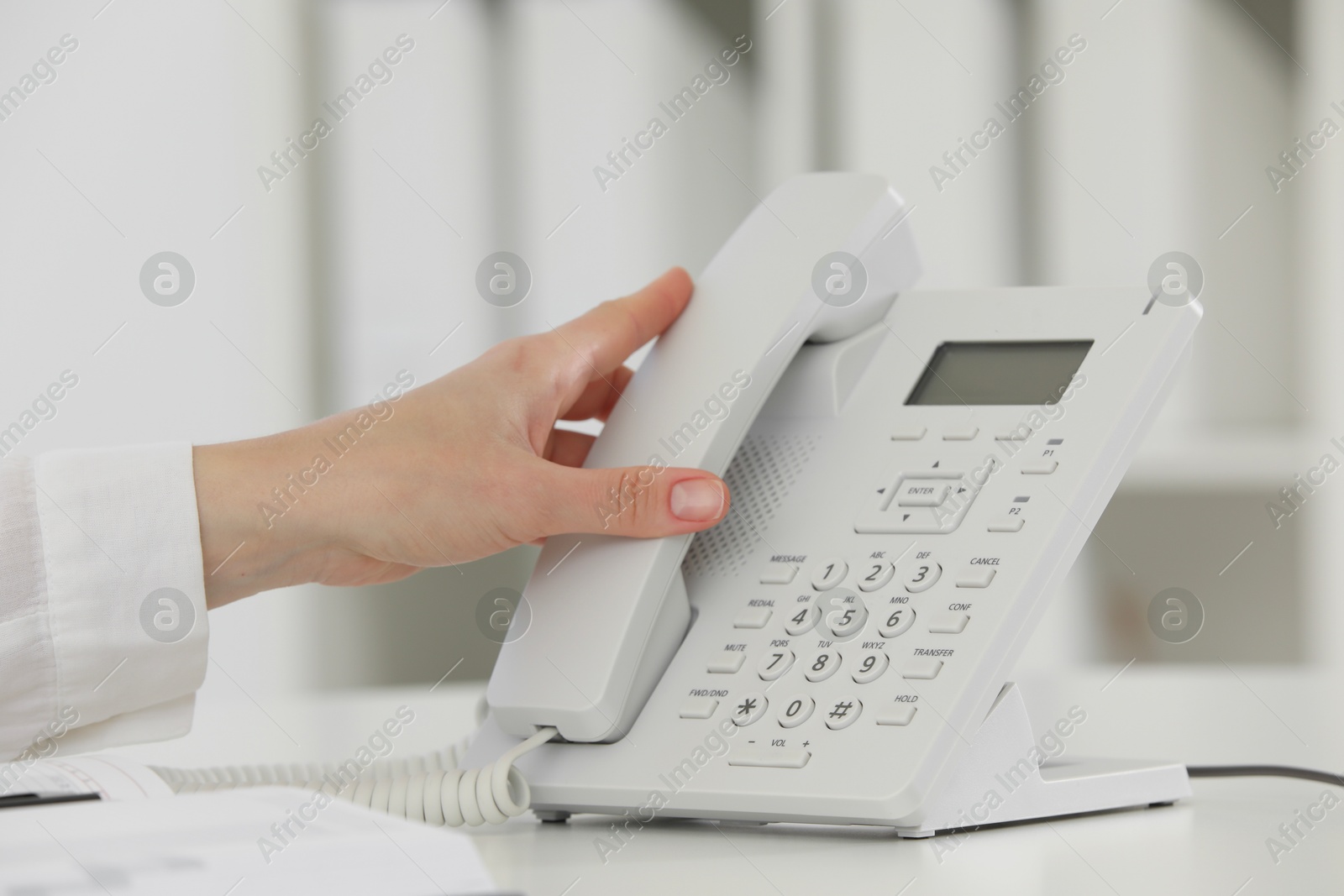 Photo of Assistant taking telephone handset at white table, closeup