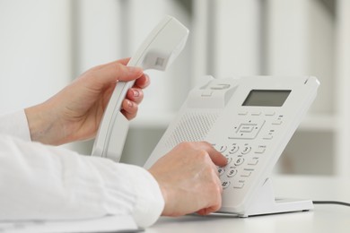 Photo of Assistant dialing number on telephone at white table, closeup