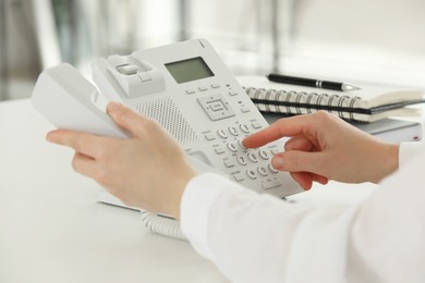 Assistant dialing number on telephone at white table, closeup