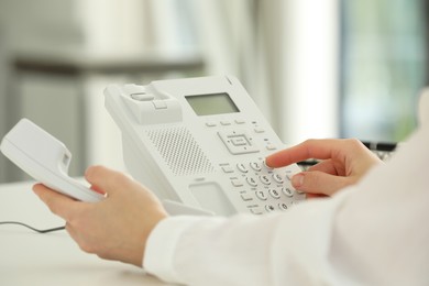 Assistant dialing number on telephone at white table, closeup