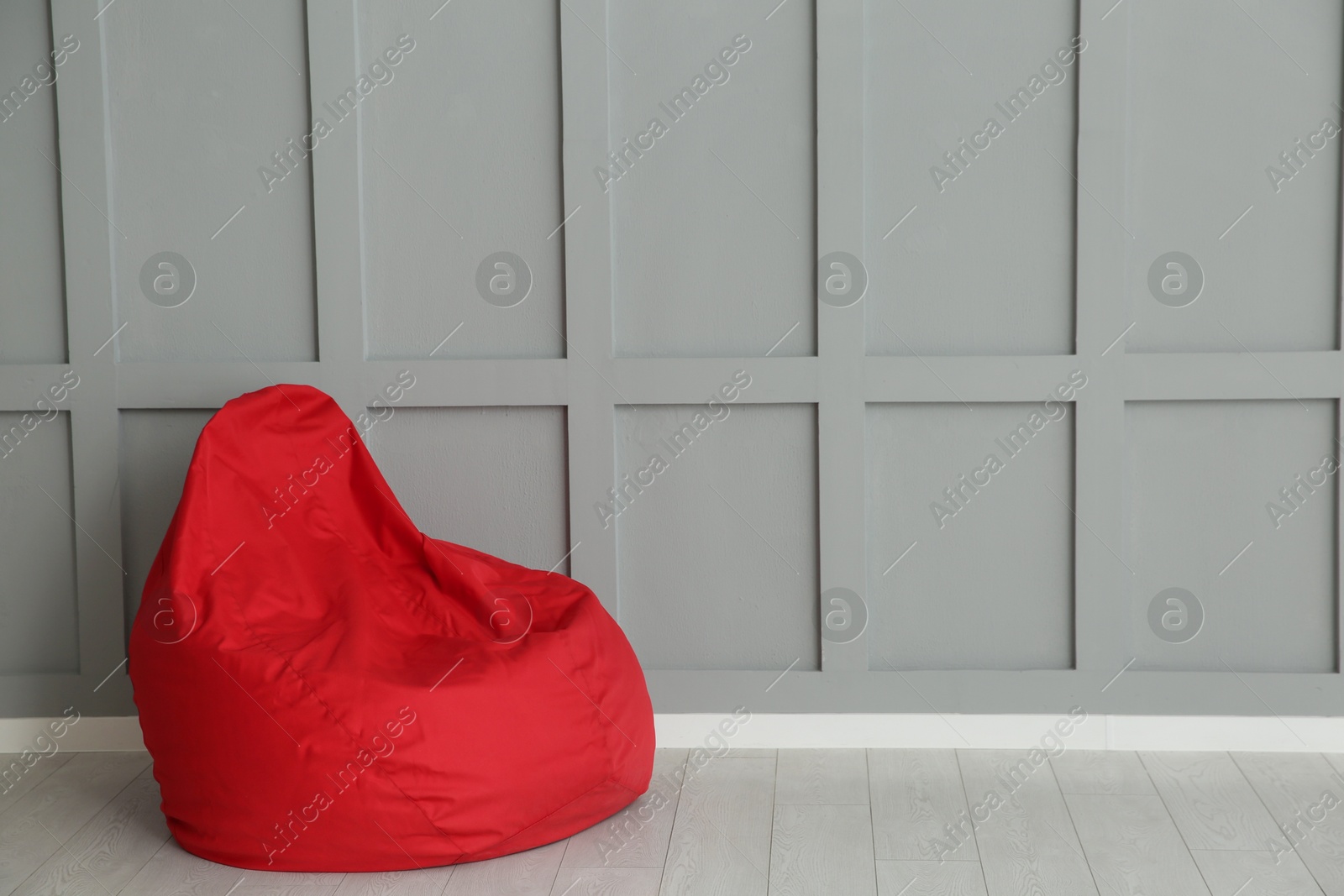 Photo of Red bean bag chair near grey wall indoors. Space for text