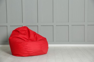 Photo of Red bean bag chair near grey wall indoors. Space for text