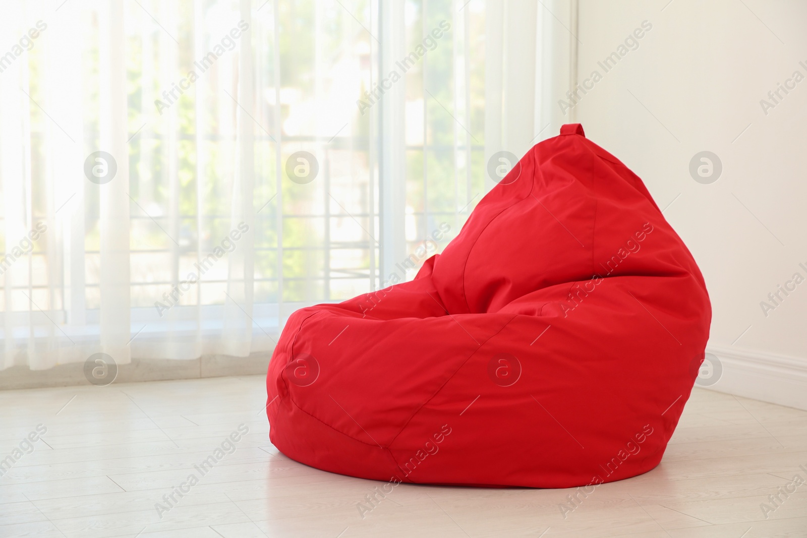 Photo of Red bean bag chair near window in room. Space for text