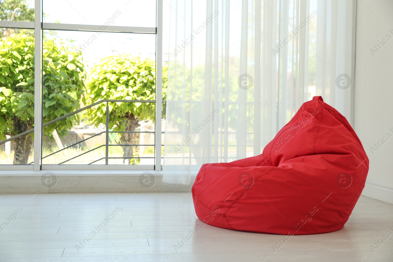 Photo of Red bean bag chair near window in room. Space for text