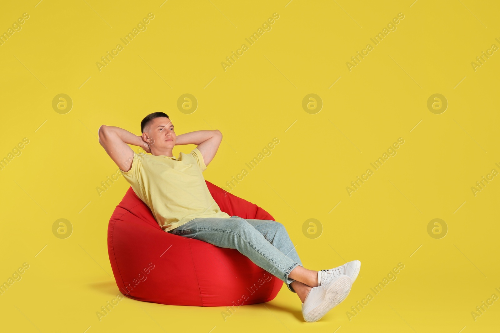 Photo of Handsome man resting on red bean bag chair against yellow background. Space for text