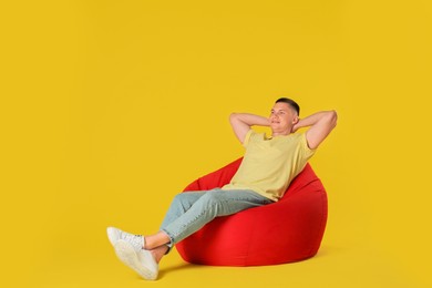 Photo of Handsome man resting on red bean bag chair against yellow background. Space for text