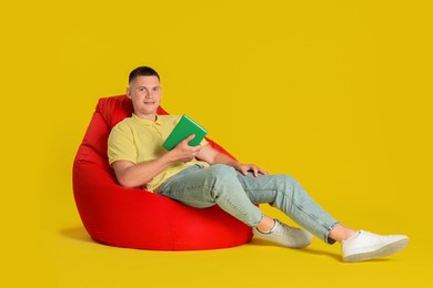 Photo of Handsome man with book on red bean bag chair against yellow background