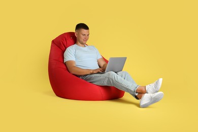 Photo of Handsome man with laptop on red bean bag chair against yellow background