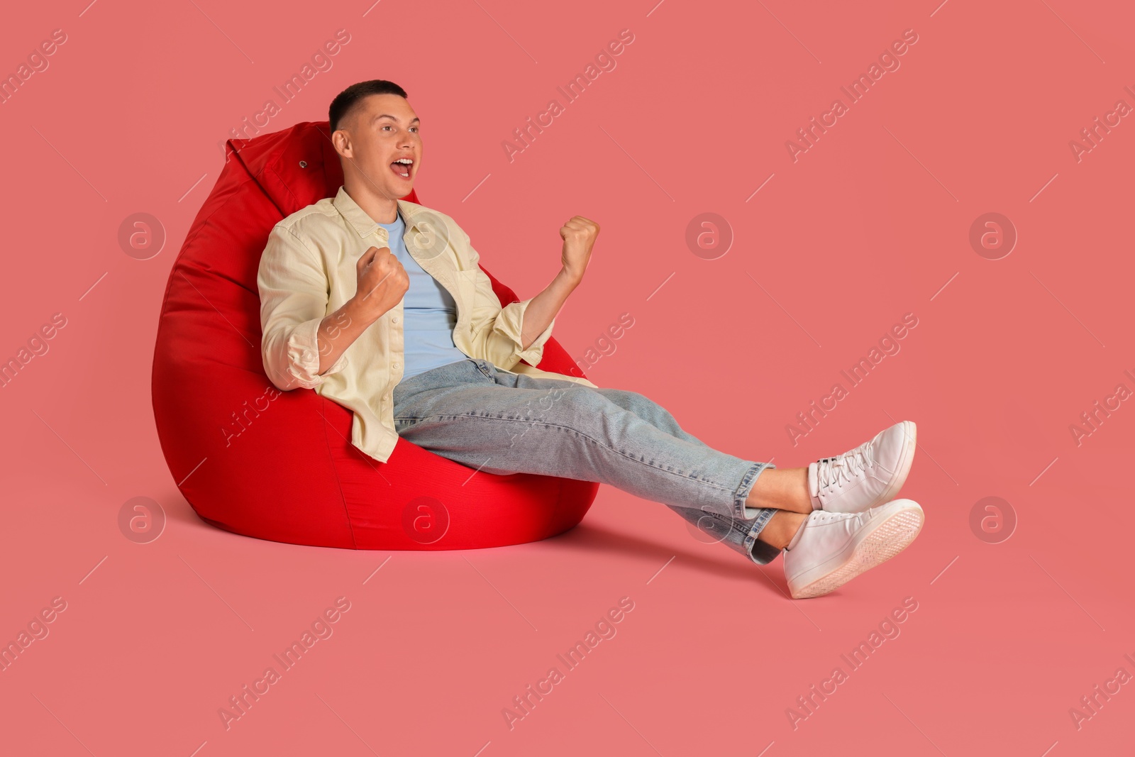 Photo of Emotional man on red bean bag chair against pink background