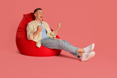 Emotional man on red bean bag chair against pink background