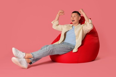 Photo of Emotional man on red bean bag chair against pink background