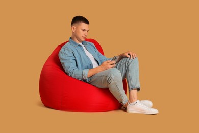 Photo of Handsome man with smartphone on red bean bag chair against beige background