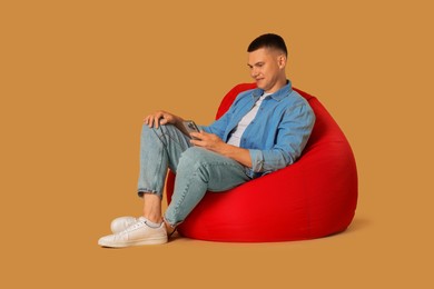 Photo of Handsome man with smartphone on red bean bag chair against beige background