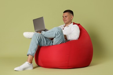 Handsome man with laptop on red bean bag chair against green background