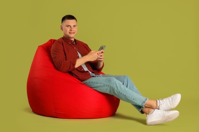 Handsome man with smartphone on red bean bag chair against green background