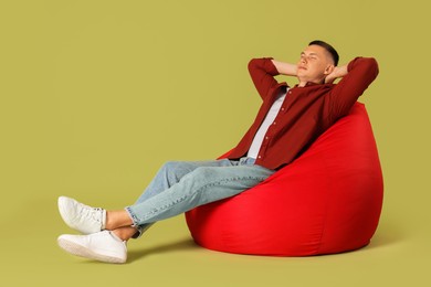 Photo of Handsome man resting on red bean bag chair against green background