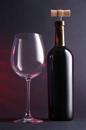 Wine bottle with corkscrew and glass in lights on grey background