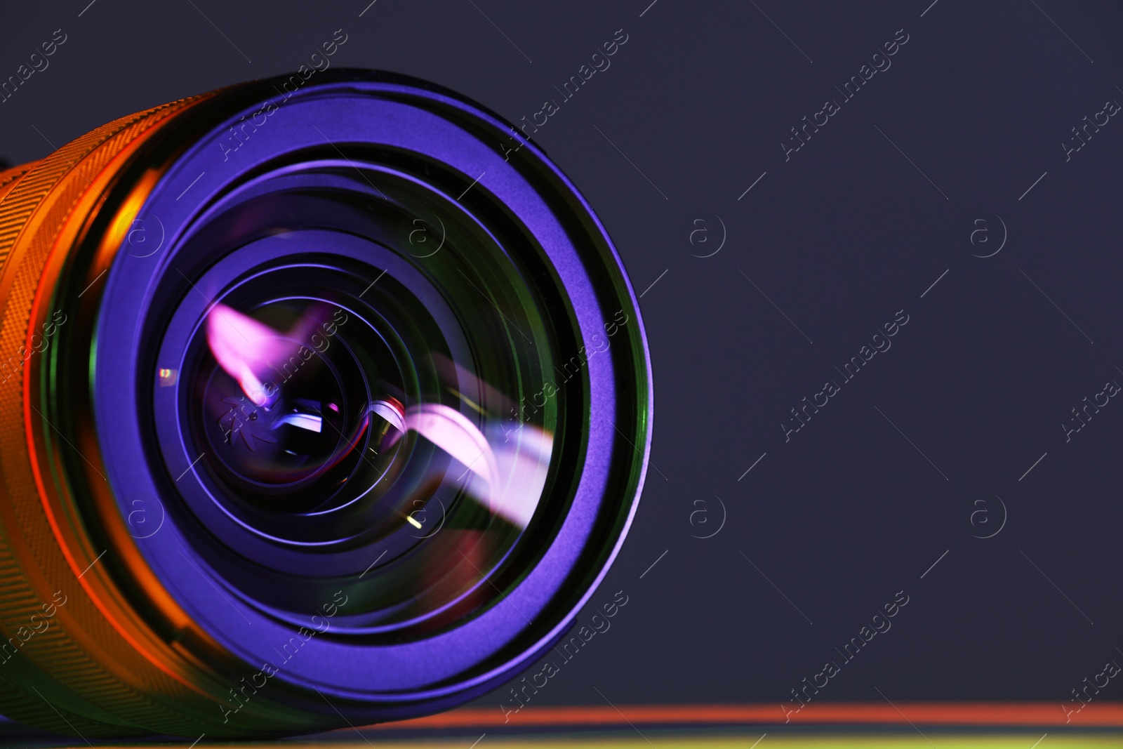 Photo of Modern camera lens in neon lights on table, closeup. Space for text