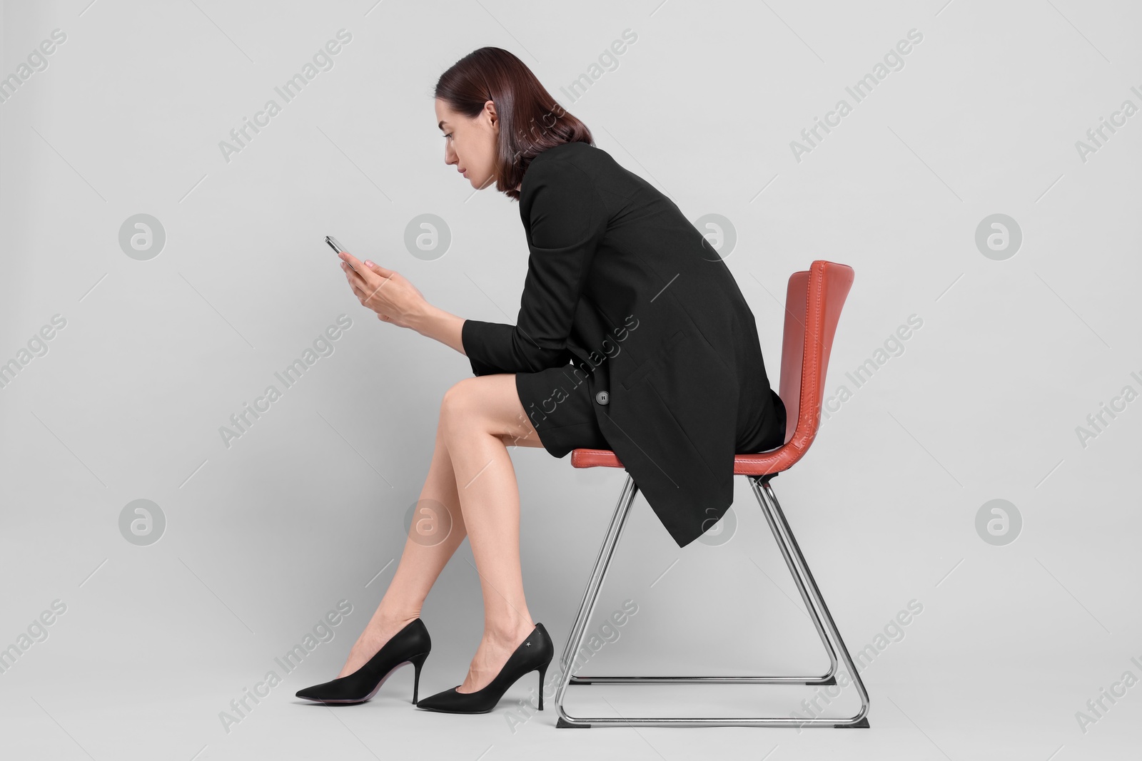 Photo of Woman with poor posture sitting on chair and using smartphone against gray background