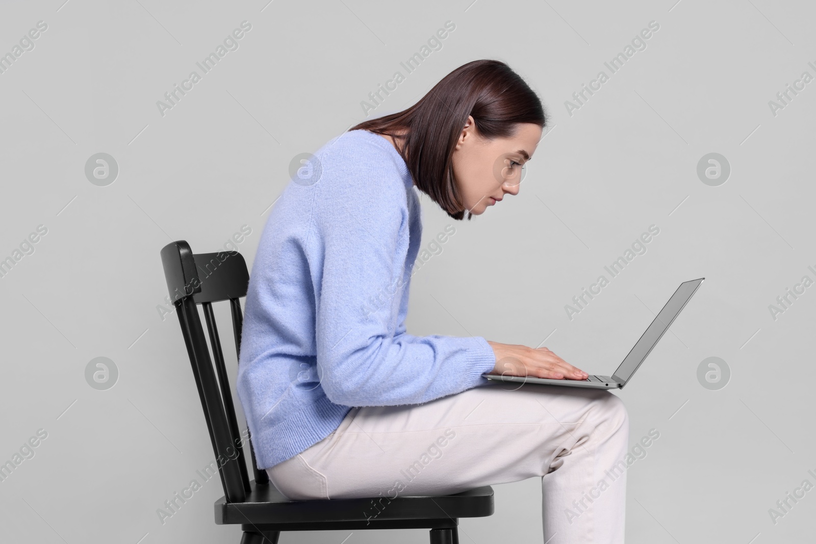 Photo of Woman with poor posture sitting on chair and using laptop against gray background