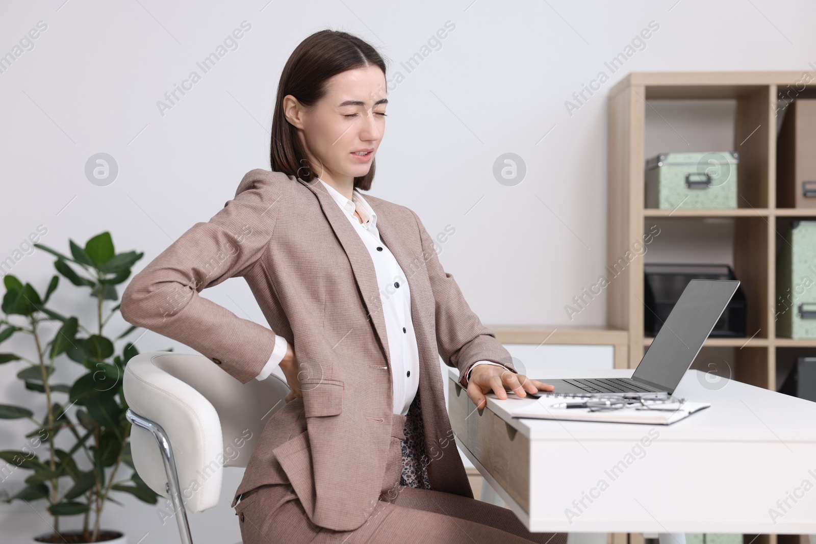 Photo of Woman suffering from back pain in office. Symptom of poor posture