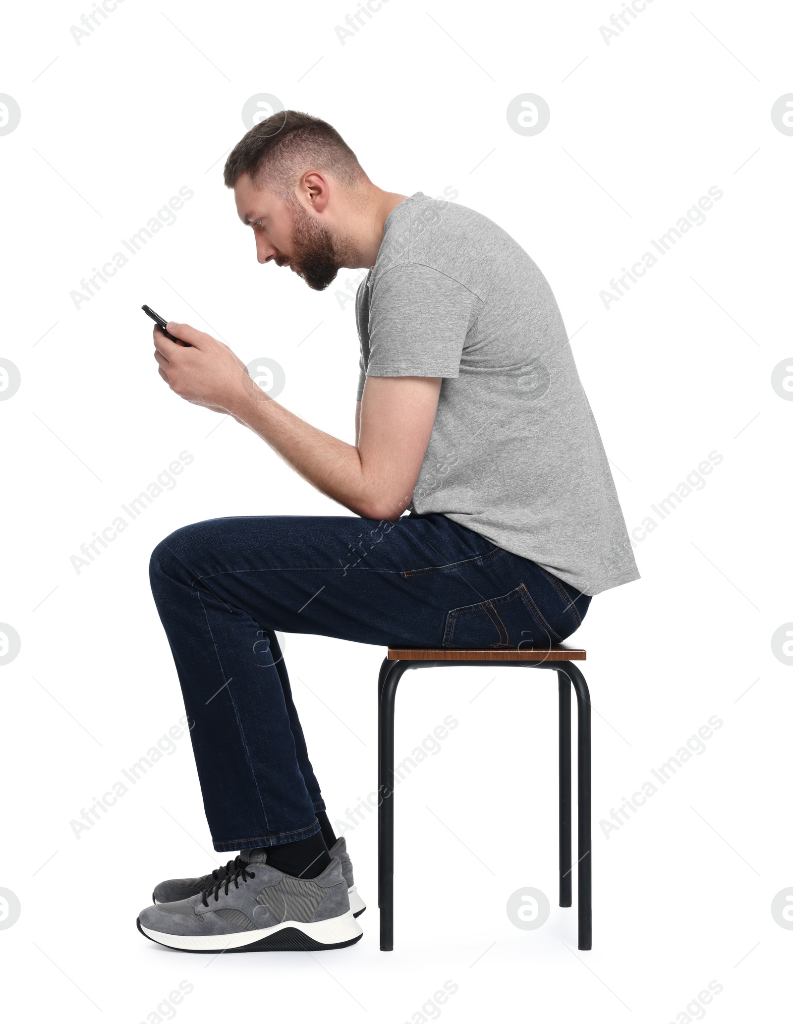 Photo of Man with poor posture sitting on chair and using smartphone against white background