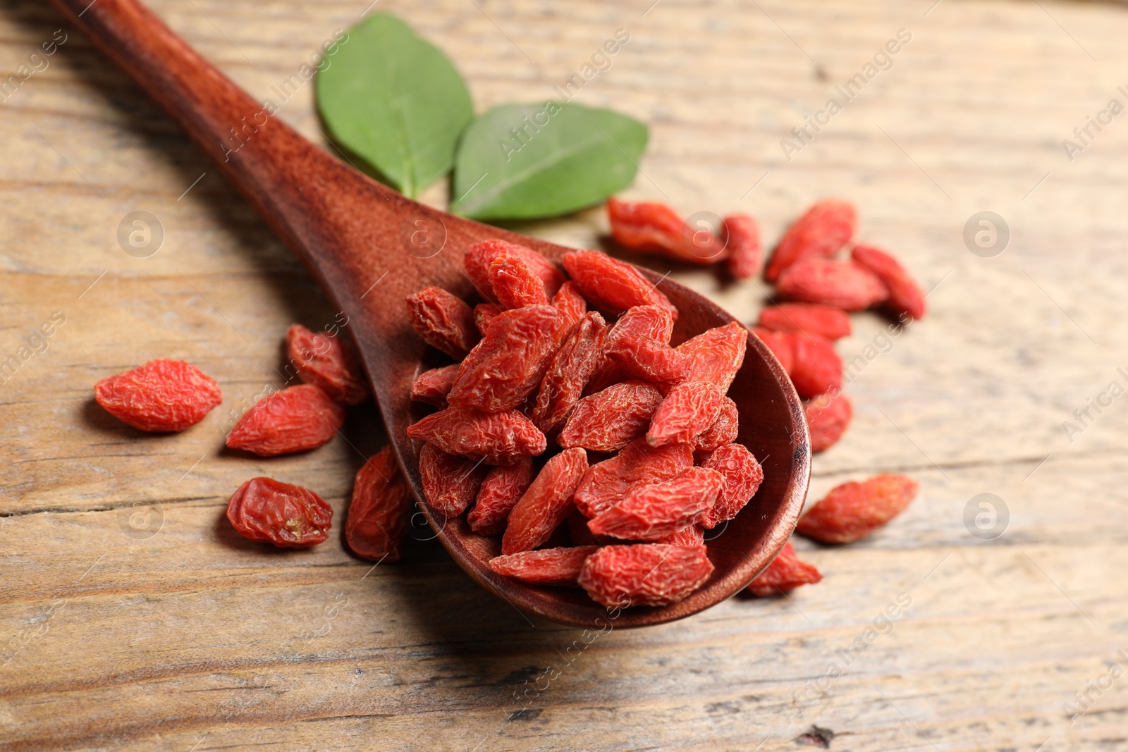 Photo of Spoon with dried goji berries on wooden table, closeup