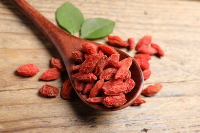 Photo of Spoon with dried goji berries on wooden table, closeup