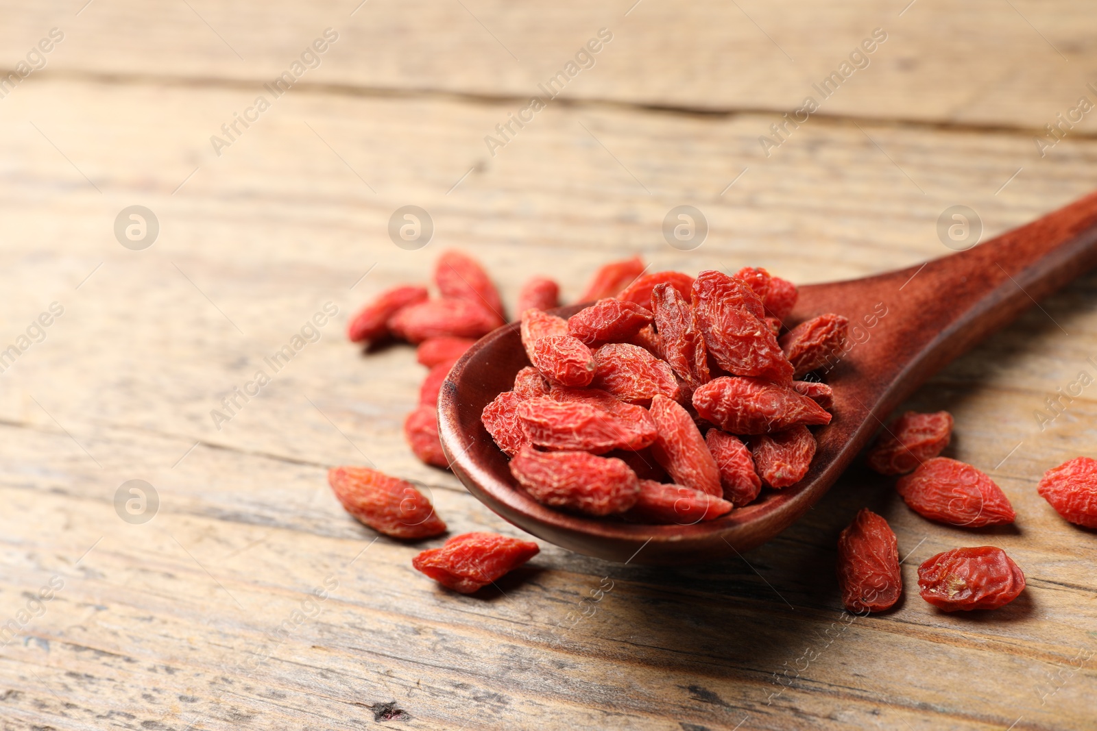Photo of Spoon with dried goji berries on wooden table, closeup. Space for text