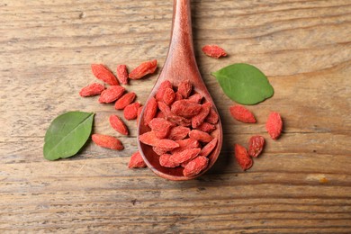 Spoon with dried goji berries and leaves on wooden table, flat lay