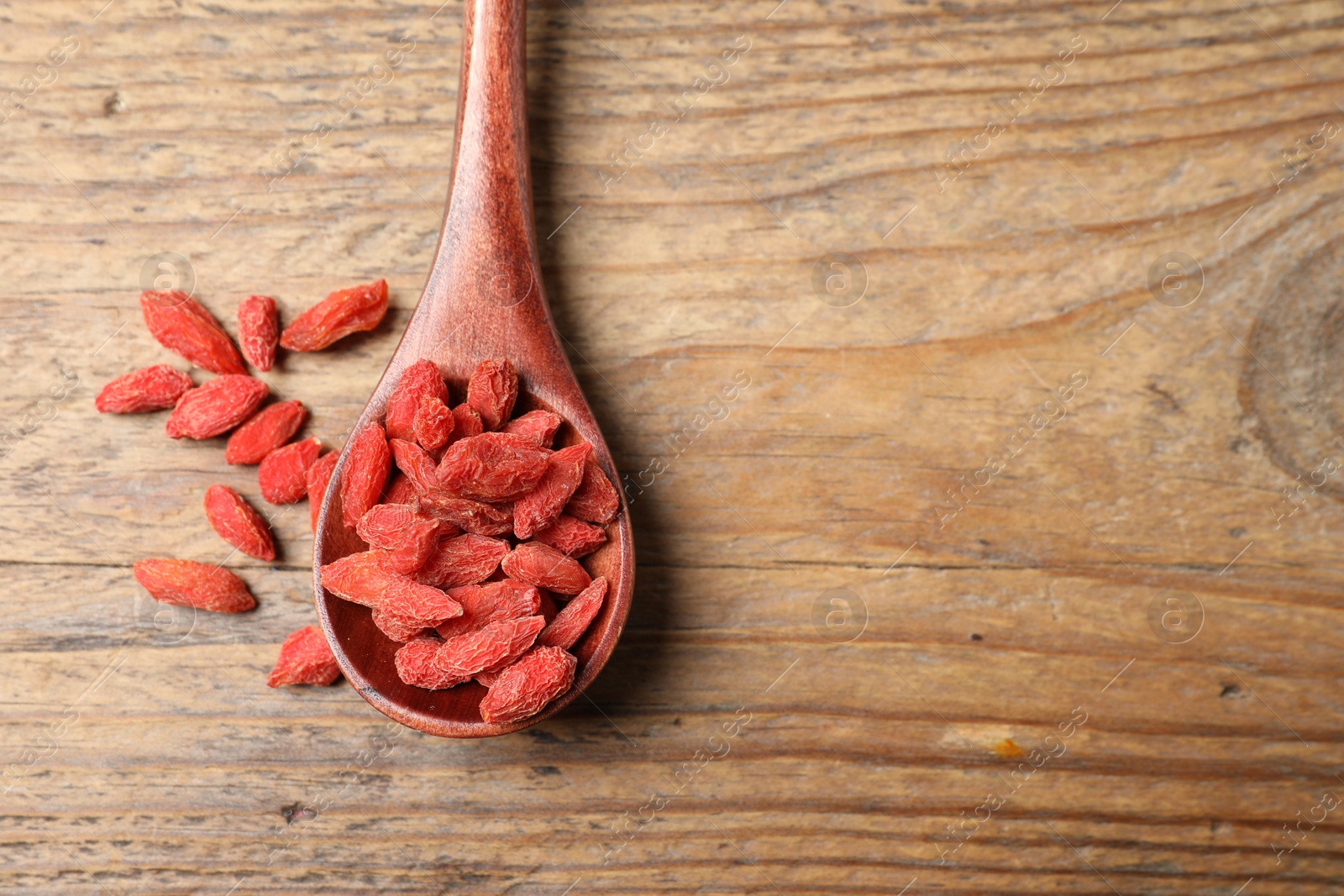 Photo of Spoon with dried goji berries on wooden table, top view. Space for text