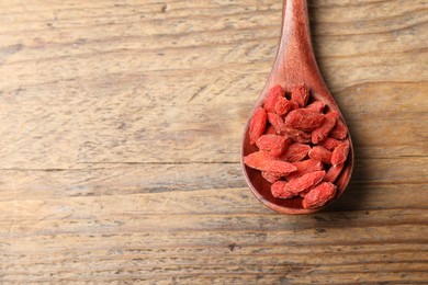 Photo of Spoon with dried goji berries on wooden table, top view. Space for text