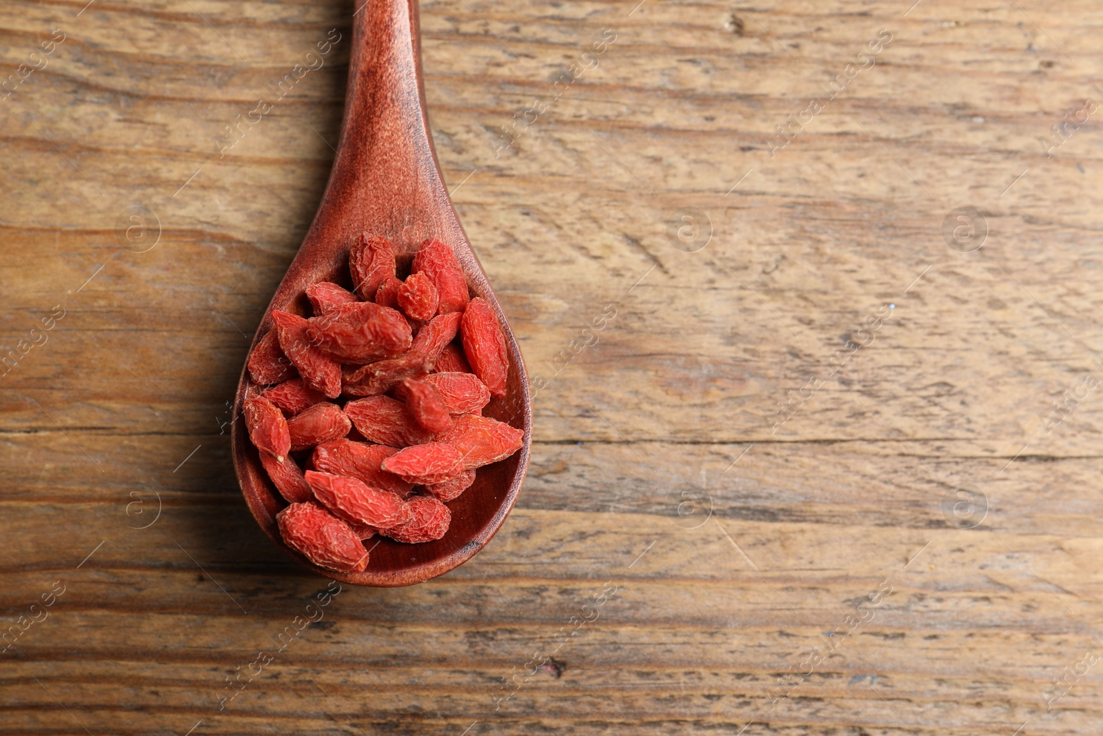 Photo of Spoon with dried goji berries on wooden table, top view. Space for text