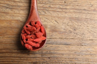 Photo of Spoon with dried goji berries on wooden table, top view. Space for text