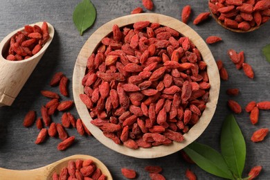 Photo of Dried goji berries, bowl, spoon and scoop on grey textured table, flat lay