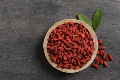 Dried goji berries in bowl and leaves on grey textured table, flat lay. Space for text