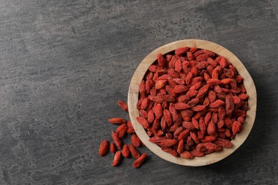 Dried goji berries in bowl on grey textured table, top view. Space for text