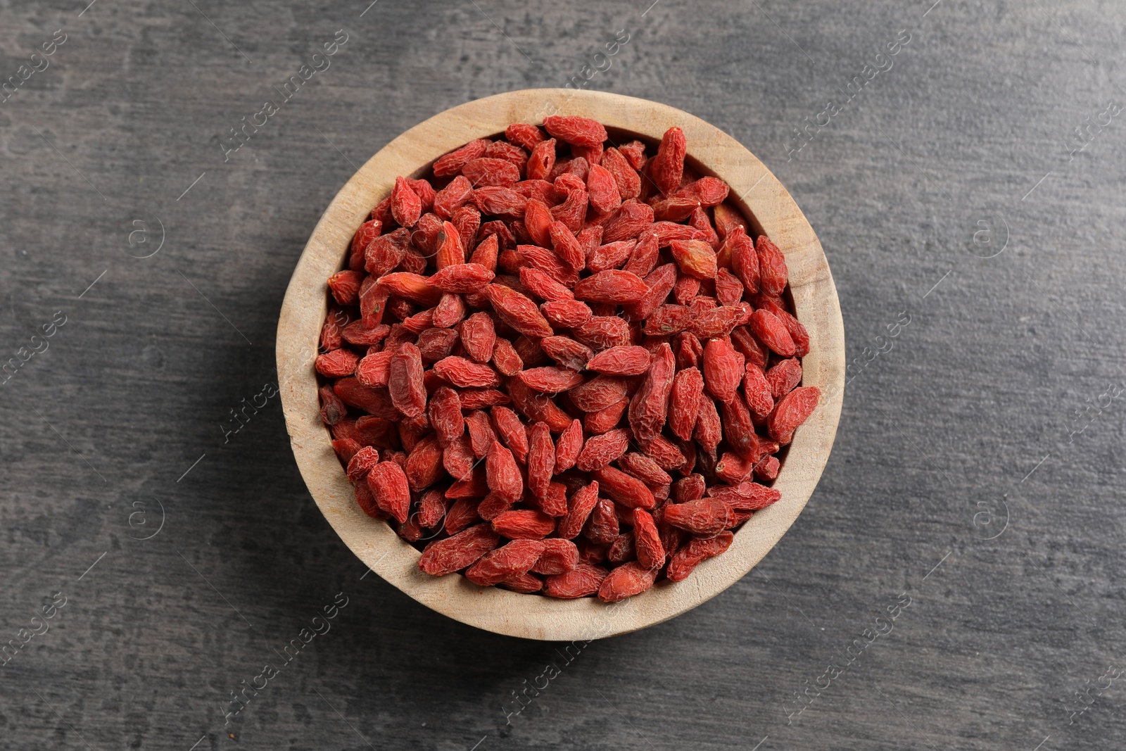 Photo of Dried goji berries in bowl on grey textured table, top view