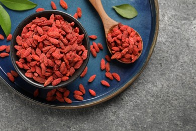 Dried goji berries in bowl and spoon on grey textured table, top view. Space for text