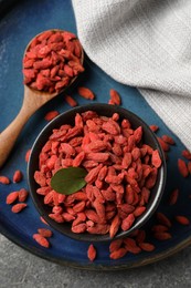 Dried goji berries in bowl and spoon on grey textured table, top view