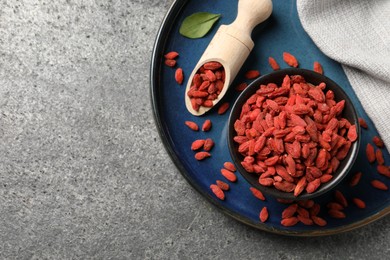 Photo of Dried goji berries in bowl and scoop on grey textured table, top view. Space for text