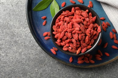 Dried goji berries in bowl on grey textured table, top view. Space for text