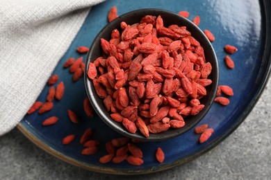 Dried goji berries in bowl on grey textured table, top view