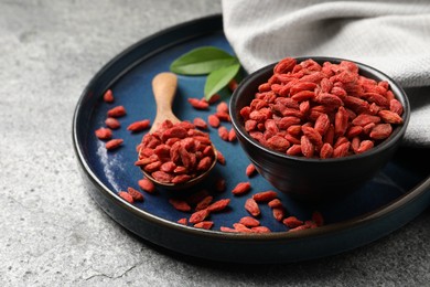 Photo of Dried goji berries in bowl and spoon on grey textured table, closeup