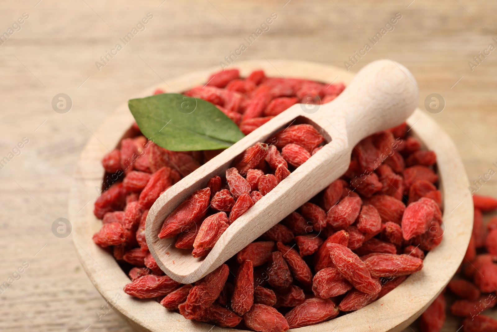 Photo of Dried goji berries in bowl and scoop on wooden table, closeup