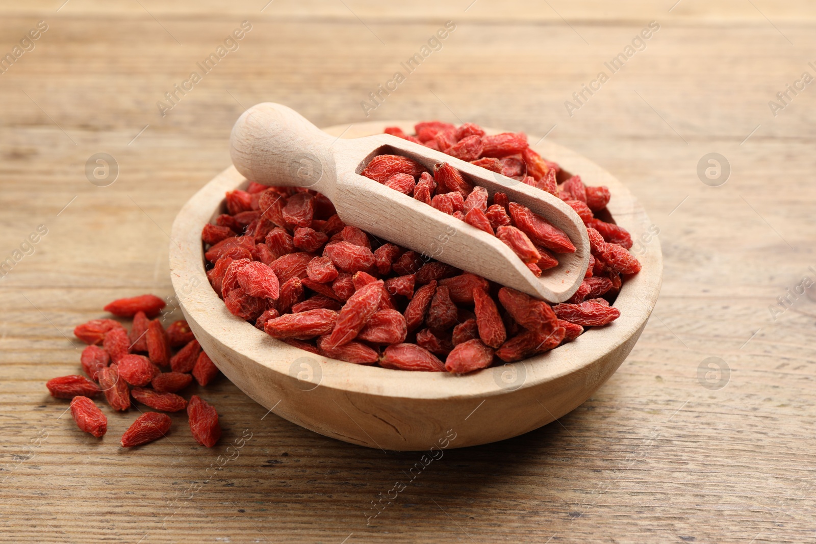 Photo of Dried goji berries in bowl and scoop on wooden table, closeup