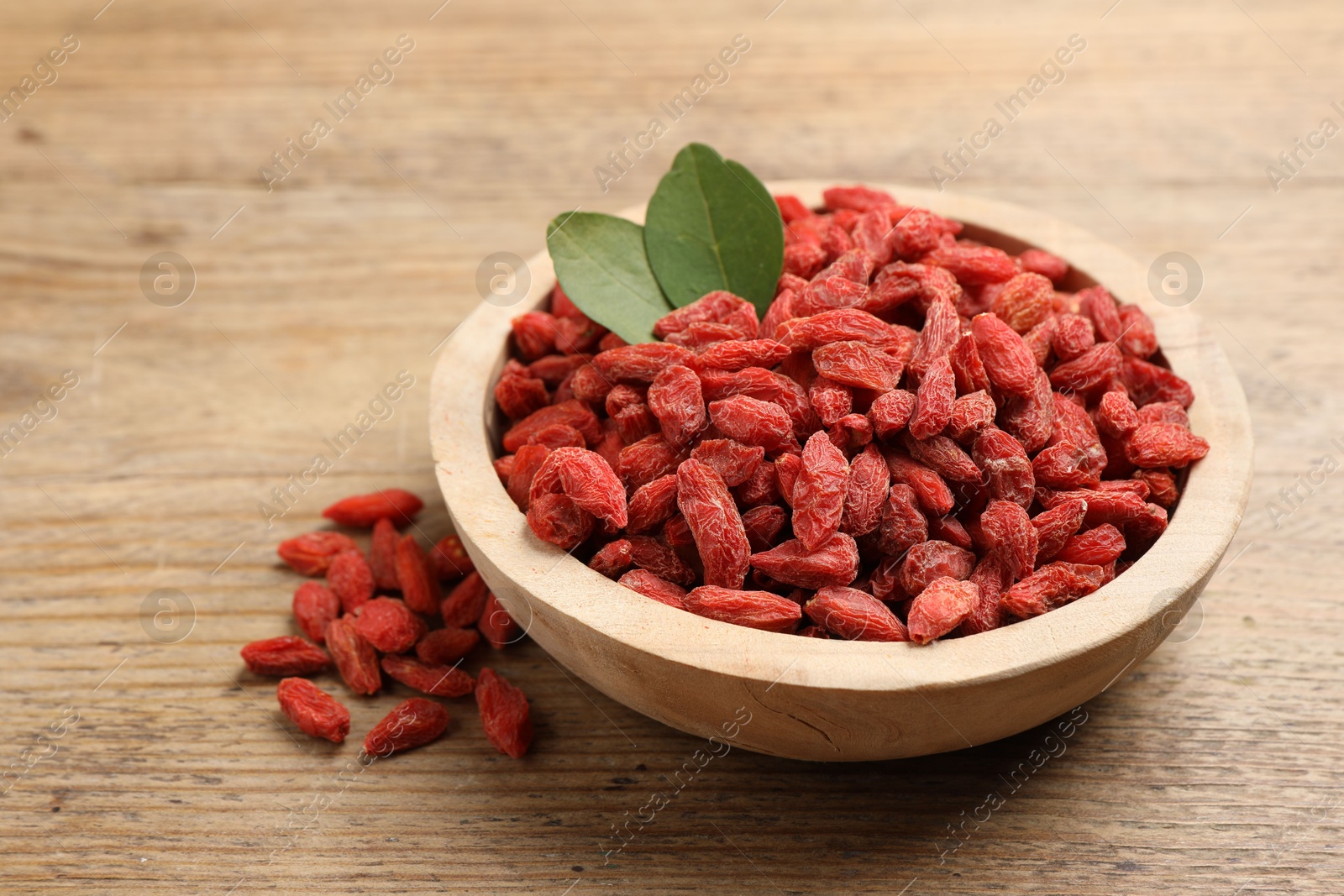 Photo of Dried goji berries and leaves in bowl on wooden table, closeup