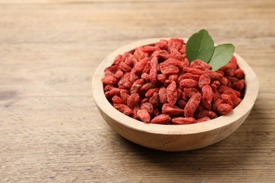 Dried goji berries and leaves in bowl on wooden table, closeup. Space for text