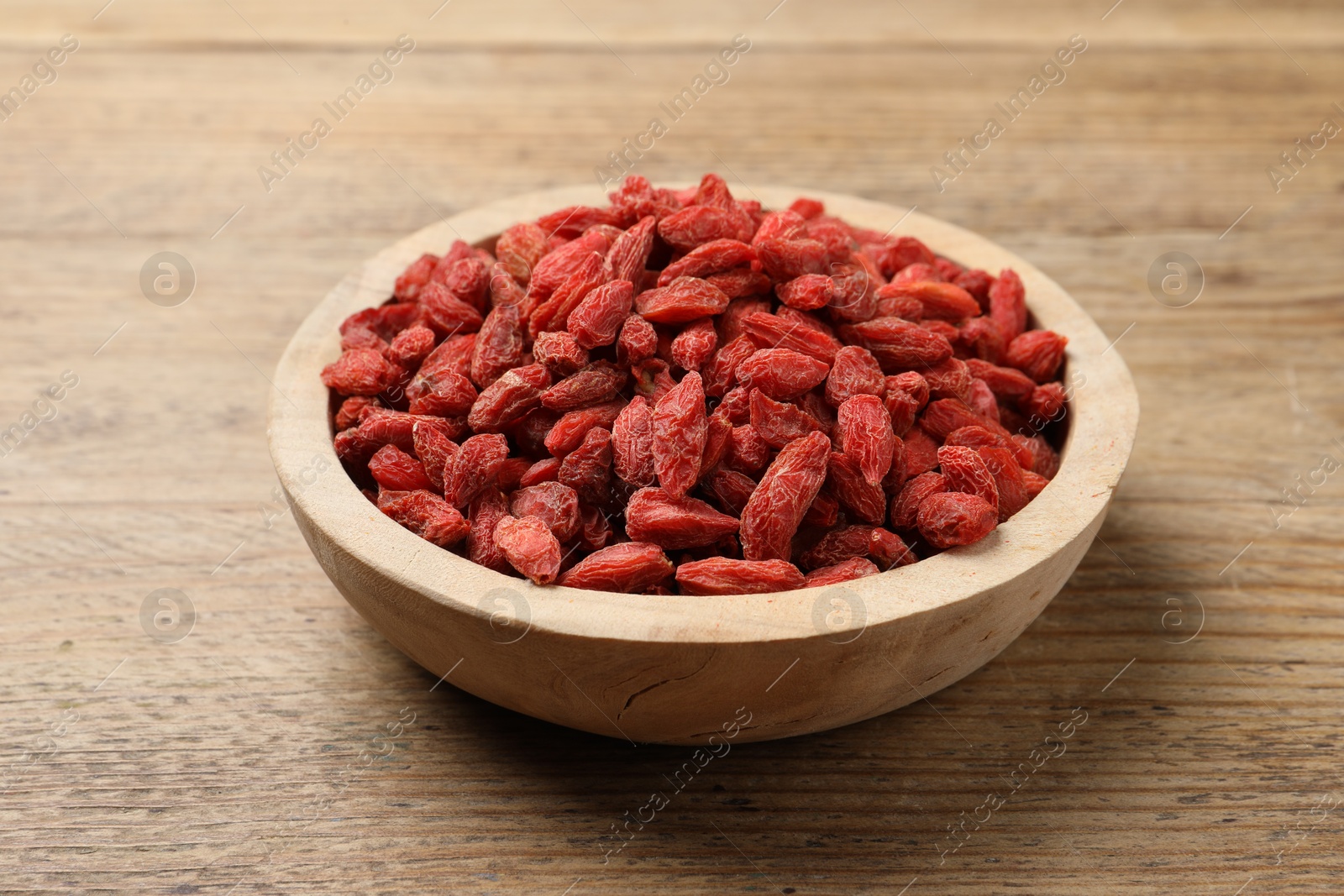 Photo of Dried goji berries in bowl on wooden table, closeup